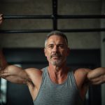 A fit and energetic man in his 50s doing a pull-up with a determined expression on his face.